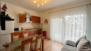 A compact kitchen with wooden cabinets, a dining table with chairs, and a grey sofa in the living area. - Lovely apartment in Vodice with WiFi (Vodice)
