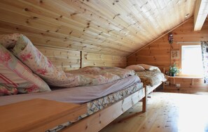 A cozy attic bedroom with a wooden sloped ceiling, a bed with floral bedding, a small table, and a window with curtains. - Lovely home in Jørpeland with house sea view (Jørpeland)