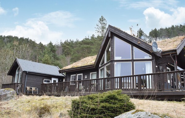 A two-story wooden cabin with large windows and a deck, surrounded by natural landscape. - Lovely home in Jørpeland with house sea view (Jørpeland)