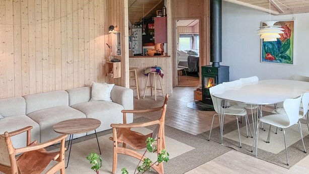 A cozy living room with a wooden wall, a sofa, a round wooden table, and a dining area with a white table and chairs. - Cozy home in Dronningmølle with WiFi (Dronningmølle)