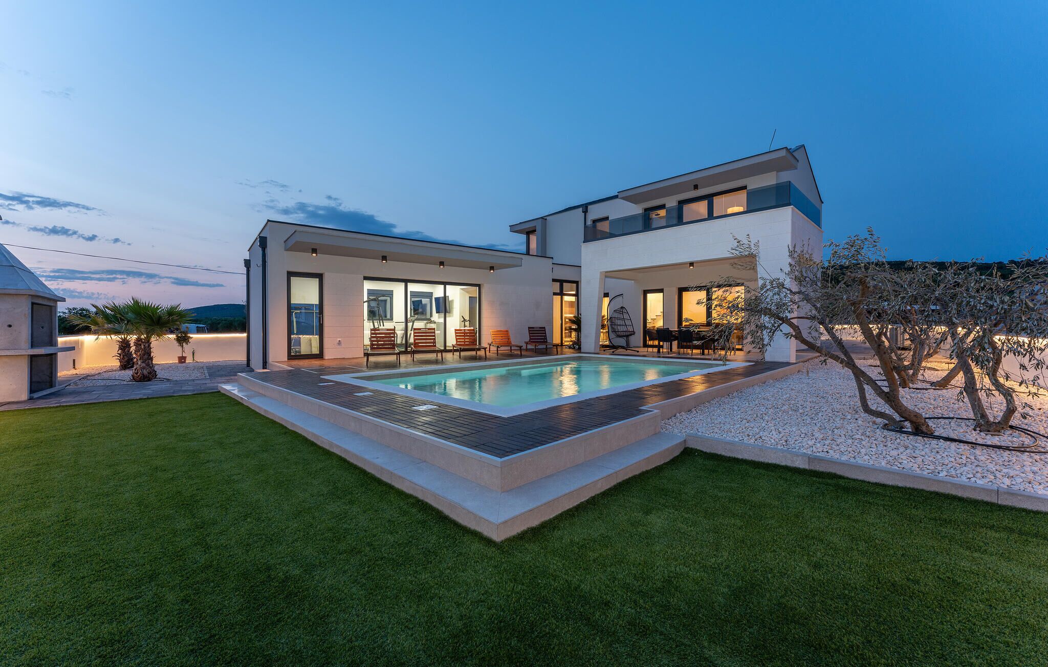 A modern two-story house with a swimming pool, a patio with outdoor furniture, and a well-maintained lawn.