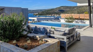 A modern outdoor pool area with a built-in seating area and a view of the sea.