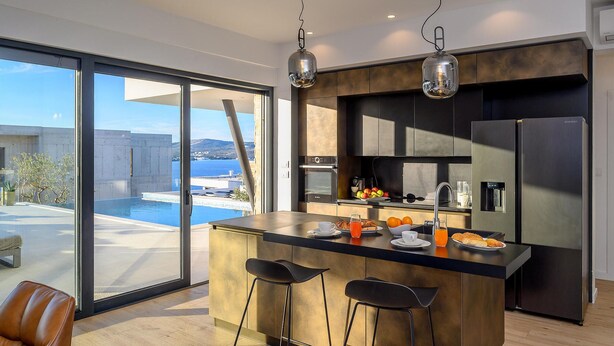 A modern kitchen with a large island, stainless steel appliances, and a view of the sea.