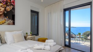 A hotel room with a bed, a painting, a window with curtains, and a view of the sea.