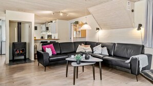 Ett modernt vardagsrum med en svart lädersoffa, ett runt soffbord och en vedkamin.