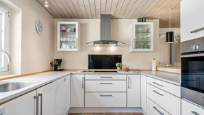 Ett modernt kök med vita skåp, en rostfri köksfläkt och en inbyggd ugn.