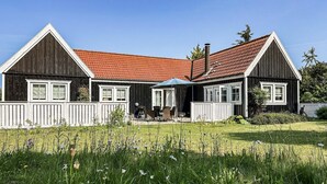 Kaksikerroksinen puutalo, jossa on punatiilinen katto, valkoiset koristeet ja katettu terassi.