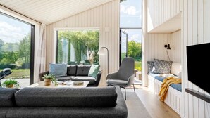 A modern living room with a large window, a sofa, a chair, and a TV. - 3 bedroom gorgeous home in Haderslev (Haderslev)