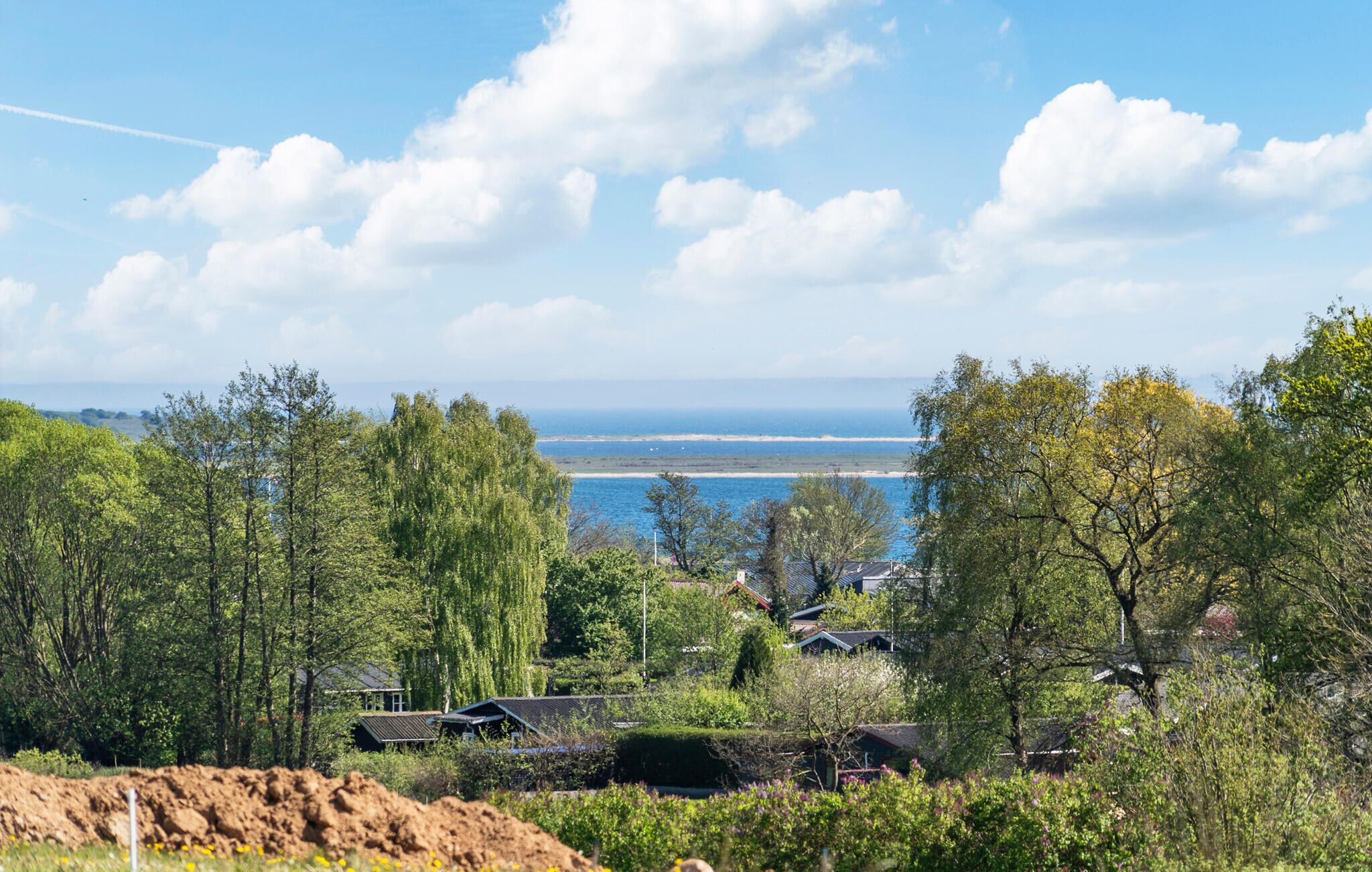 A coastal landscape with a clear view of the sea, surrounded by trees and residential buildings.