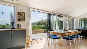 A modern kitchen with a wooden countertop, a coffee maker, and a kettle. There is a dining area with a wooden table and blue chairs. The room has large windows with a view of greenery outside. - 3 bedroom gorgeous home in Haderslev (Haderslev)