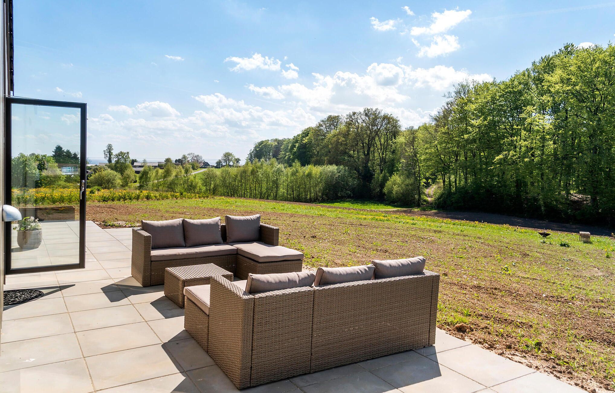 Een terras met rieten meubels en een glazen deur naar een tuin.