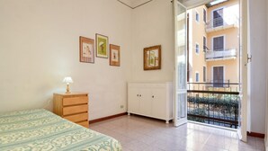 A bedroom with a bed, a nightstand, a cabinet, and a balcony with a view of a building.