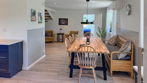 A modern kitchen with a wooden dining table, chairs, and a built-in bench. There is a staircase leading to an upper level, and a large window providing natural light. - Cozy home in Bolmsö with sauna (Bolmsö)