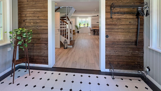 A hallway with a wooden wall, a staircase, and a dining area in the background. - Cozy home in Bolmsö with sauna (Bolmsö)