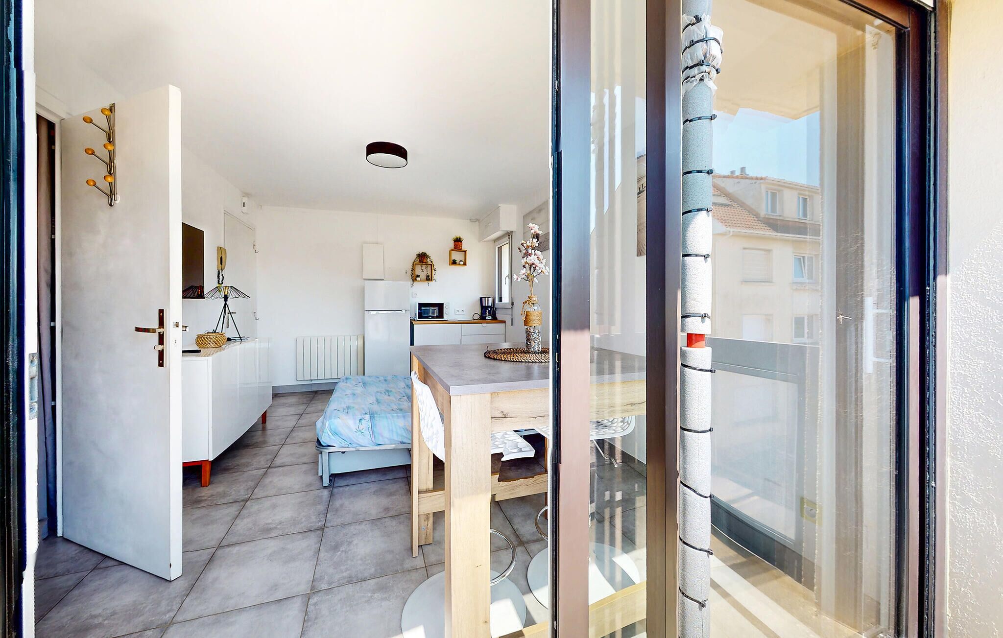 Une pièce compacte et bien éclairée, comprenant un lit, une petite kitchenette et un coin repas.