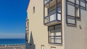 Een meerhoog gebouw met grote ramen en balkons, gelegen nabij een waterkant met een helderblauwe lucht.