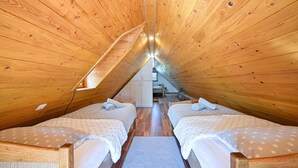 A cozy attic bedroom with two beds, wooden walls, a sloped ceiling, and a small window.