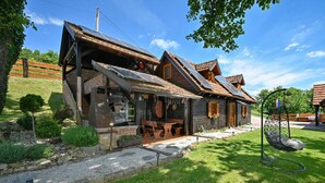 A rustic wooden house with a stone foundation, a wooden porch, and a stone pathway leading to the entrance.