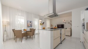 Una cocina moderna con una isla central, armarios blancos y un comedor con sillas de mimbre.