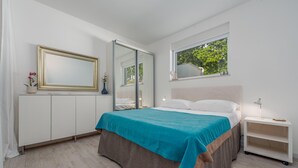 Un dormitorio moderno con cama, mesitas de noche, un espejo y una ventana con vistas a árboles.