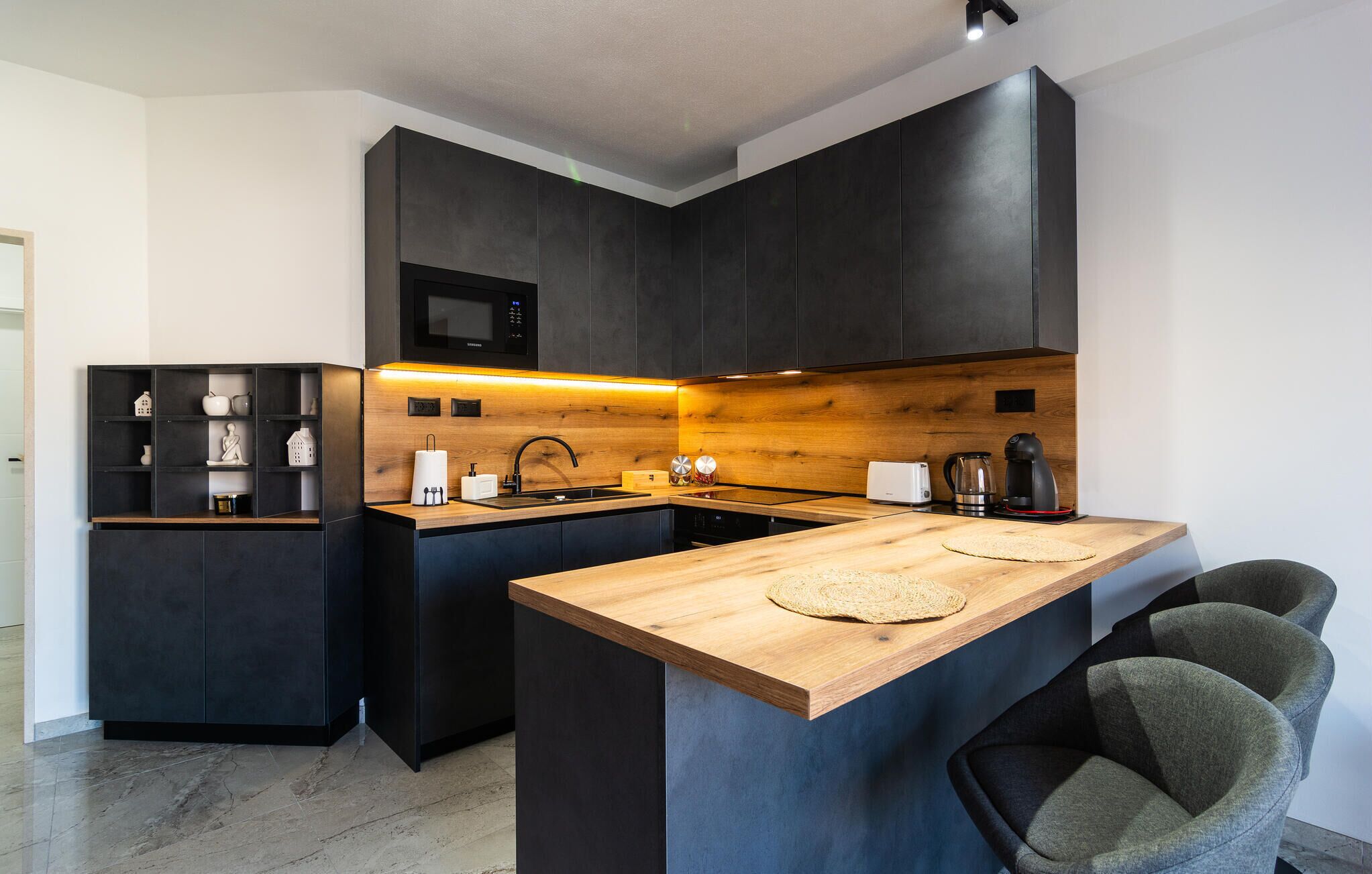 Cozinha moderna com armários escuros, ilha de madeira e micro-ondas embutido.
