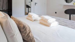 A neatly made bed with white linens and a folded towel, a brown pillow, and a white wall with a round mirror and a small shelf with a yellow object. - 1 bedroom stunning apartment in Hvar (Hvar)