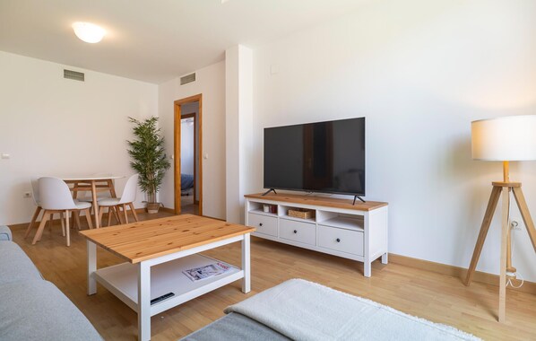 Un salon moderne avec une table basse en bois, un téléviseur posé sur un meuble blanc, une lampe et une plante en pot.