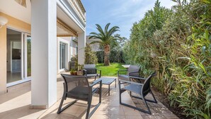 A patio with outdoor furniture, a view of the garden, and a building with a white exterior.