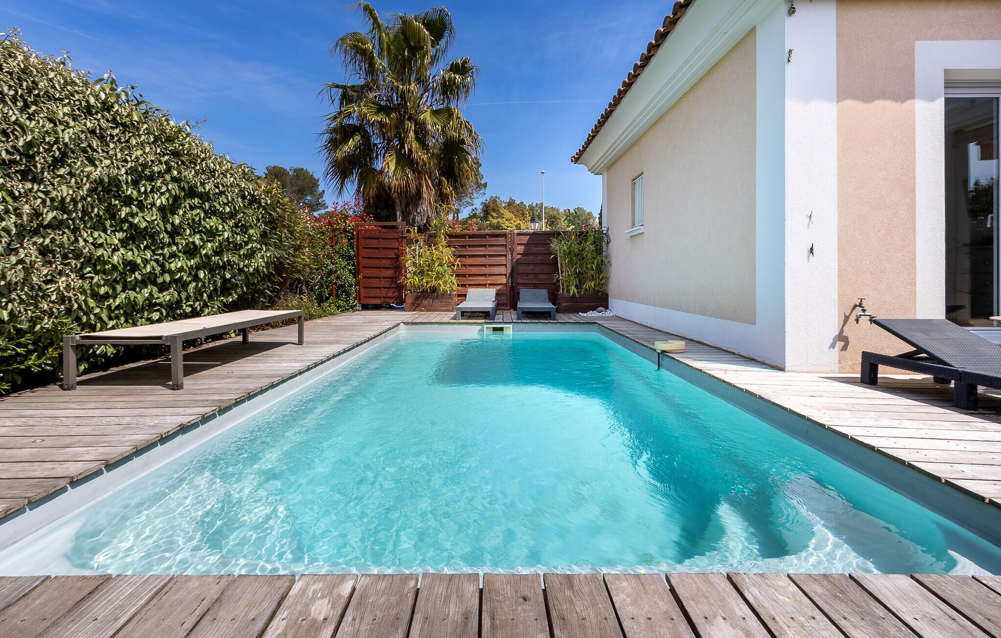 Ein rechteckiger Pool mit Holzdeckbelag, umgeben von einem Holenzaun und üppiger Bepflanzung.