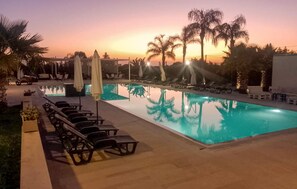 A swimming pool with lounge chairs and umbrellas, surrounded by palm trees and a sunset view. - Gorgeous home in Acate (Acate)