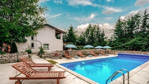 Una piscina amb gandules i ombrelles, envoltada per una paret de pedra i arbres.