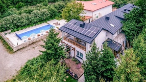 Una casa moderna amb piscina, panells solars i terrassa de fusta.