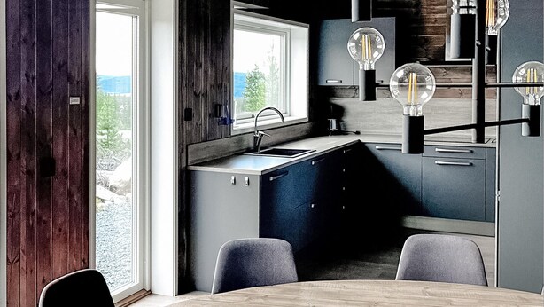 Een moderne keuken met raam, spoelbak en een eethoek met stoelen.