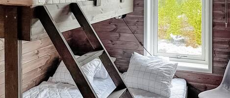 Una cama litera con escalera de madera, ropa de cama blanca y una ventana con vista a árboles.