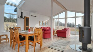 Tilava huone, jossa on puinen ruokapöytä ja -tuolit, punainen sohva ja suuri ikkuna, josta avautuu näkymä ulos.