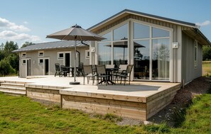 Une maison moderne dotée d’une grande terrasse, de mobilier d’extérieur et de larges fenêtres.