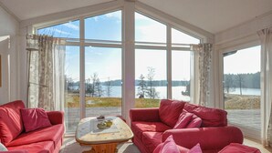 Huoneessa on suuret ikkunat, punainen sohva, puinen sohvapöytä ja näkymä järvelle.