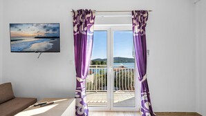 A room with a large window, a sofa, a remote control, and a painting of a beach scene. - Gorgeous apartment in Pirovac with WiFi (Pirovac)