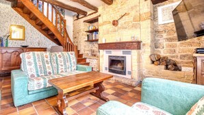 A cozy living room with a stone fireplace, a wooden staircase, and a sofa with patterned cushions.