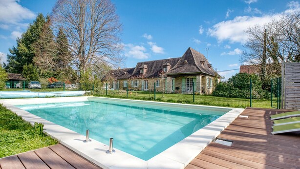 A rectangular swimming pool with a wooden deck, surrounded by a grassy area and trees.