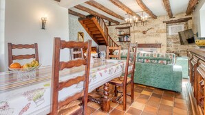 A rustic room with exposed wooden beams, a dining table with a floral tablecloth, a green upholstered sofa, and a stone wall.