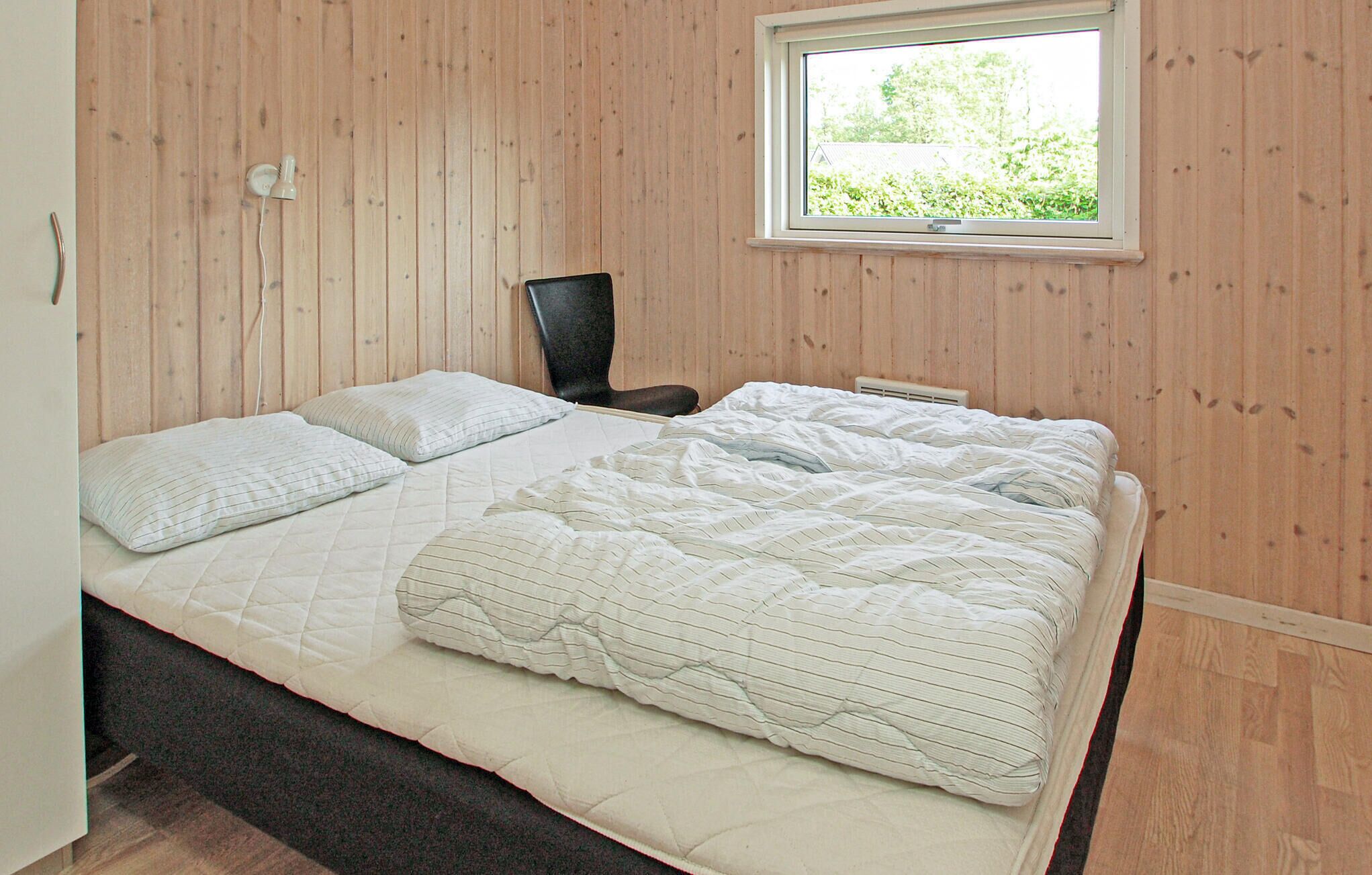 Ein Schlafzimmer mit Bett, Kissen, einem Sessel, einem Fenster und Holzwänden.
