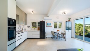 A modern kitchen with a dining area, large windows, and a view of the outdoors.