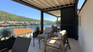 A balcony with a view of a river and houses, furnished with chairs and a table.