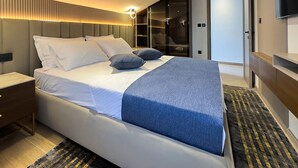 A modern hotel room with a large bed, a bedside table, a wardrobe, and a television.