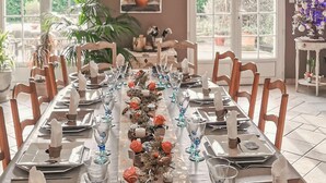 Una larga mesa de comedor dispuesta con copas y centros de mesa florales, rodeada de sillas de madera.
