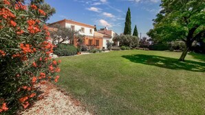 Una casa de dos pisos con techo de tejas, rodeada de un césped cuidado y varios arbustos.