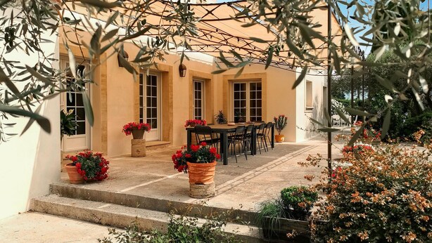 Un patio con una mesa y sillas, rodeado de plantas y flores en macetas.