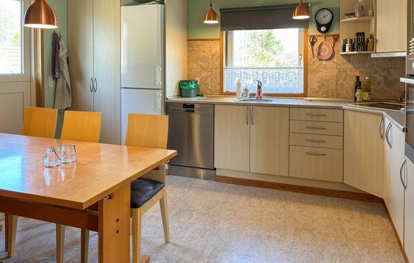 Une cuisine avec une table en bois, des chaises, un lave-vaisselle et une fenêtre donnant sur un paysage verdoyant.