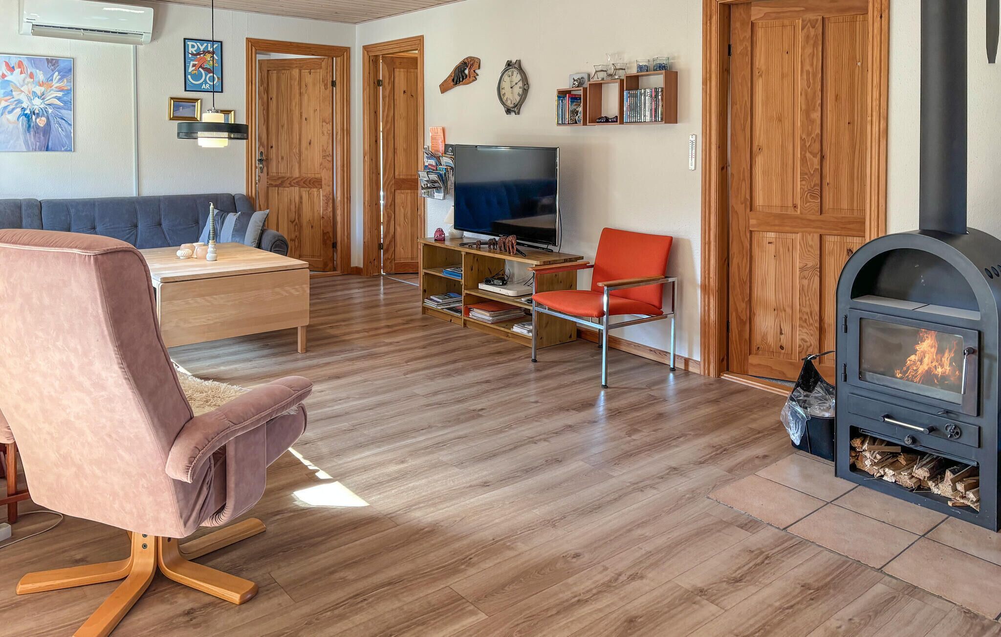 A living room with a sofa, a chair, a TV, a bookshelf, and a wood-burning stove.